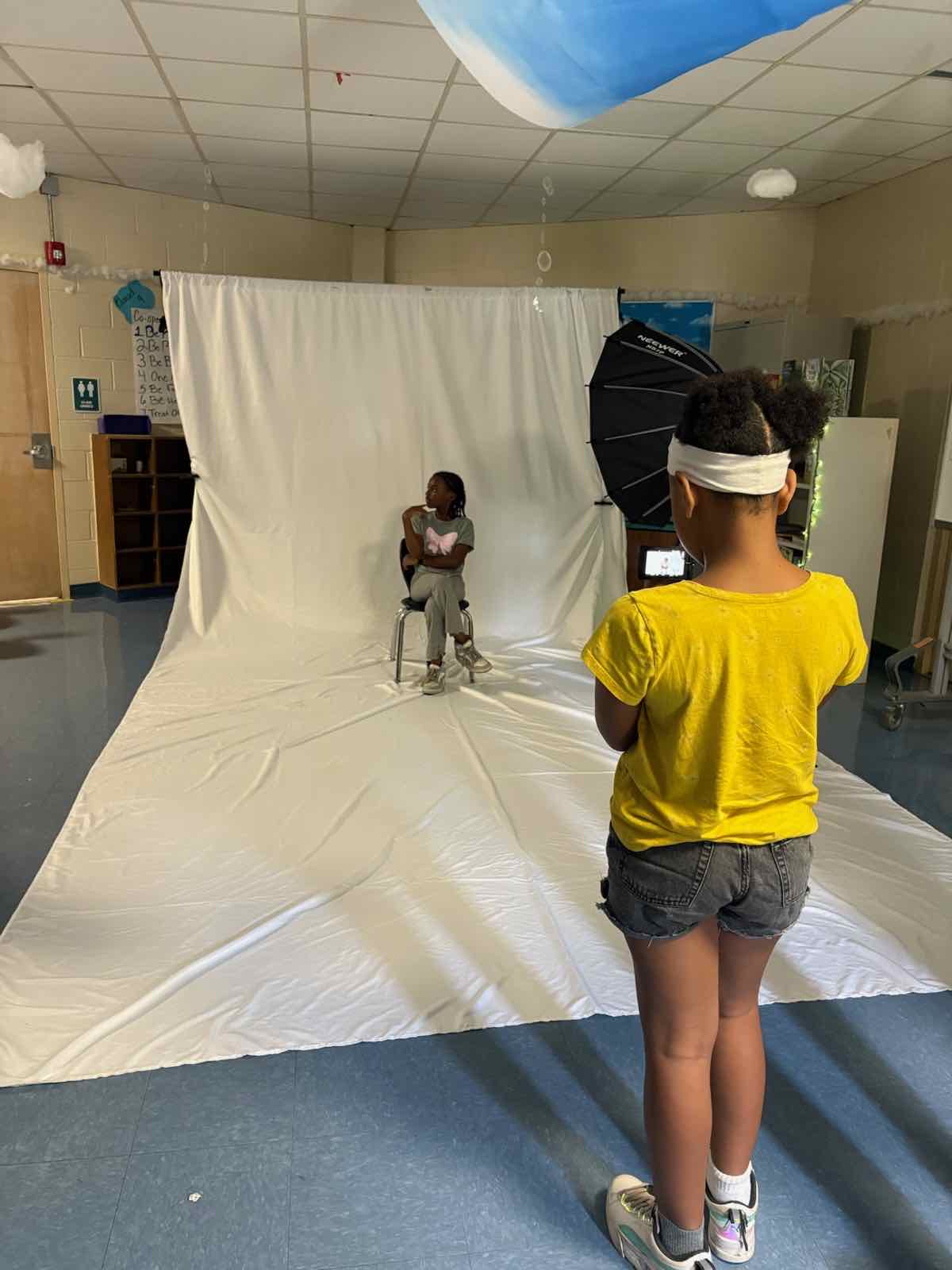 A Creator Bound Scholar in a yellow shirt photographing another Scholar on a white backdrop
